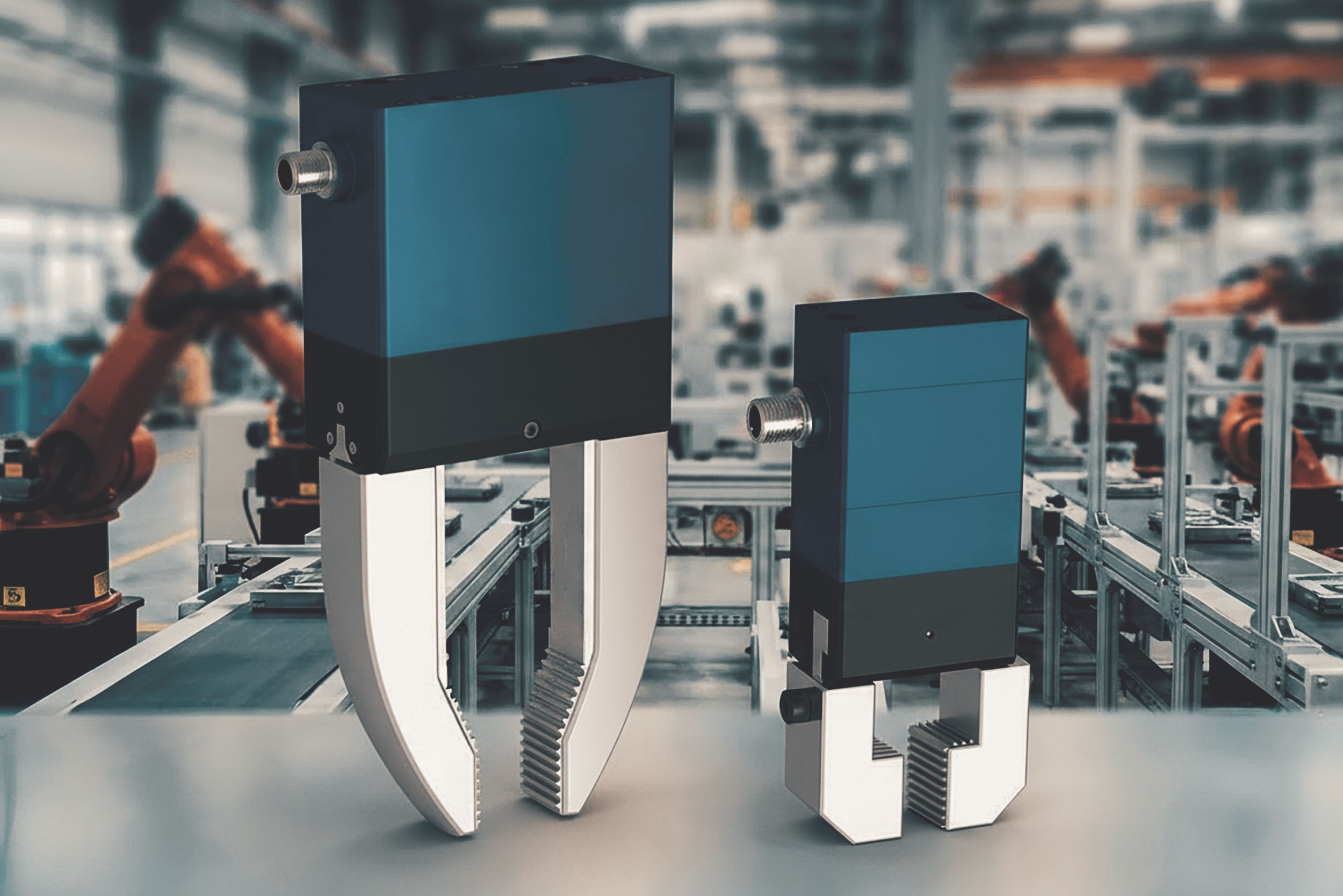 Two mechatronic gripper modules with blue housings and metallic gripping arms in a production environment with industrial robots in the background