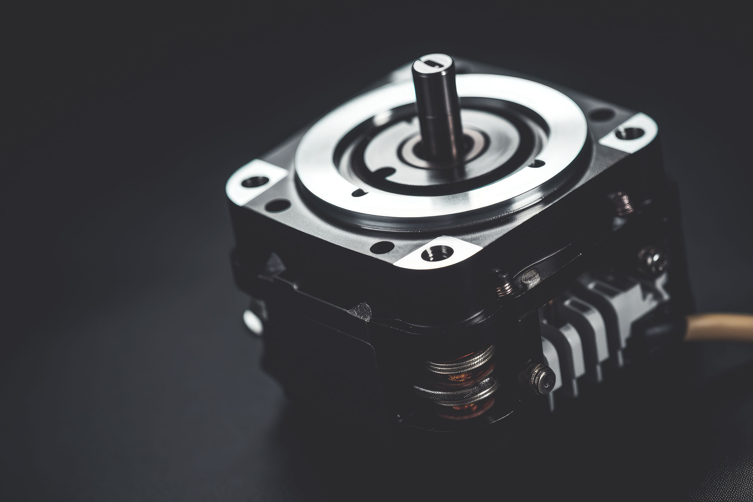 Nahaufnahme eines Servomotors mit sichtbarer Welle und Befestigungslöchern auf dunklem Hintergrund