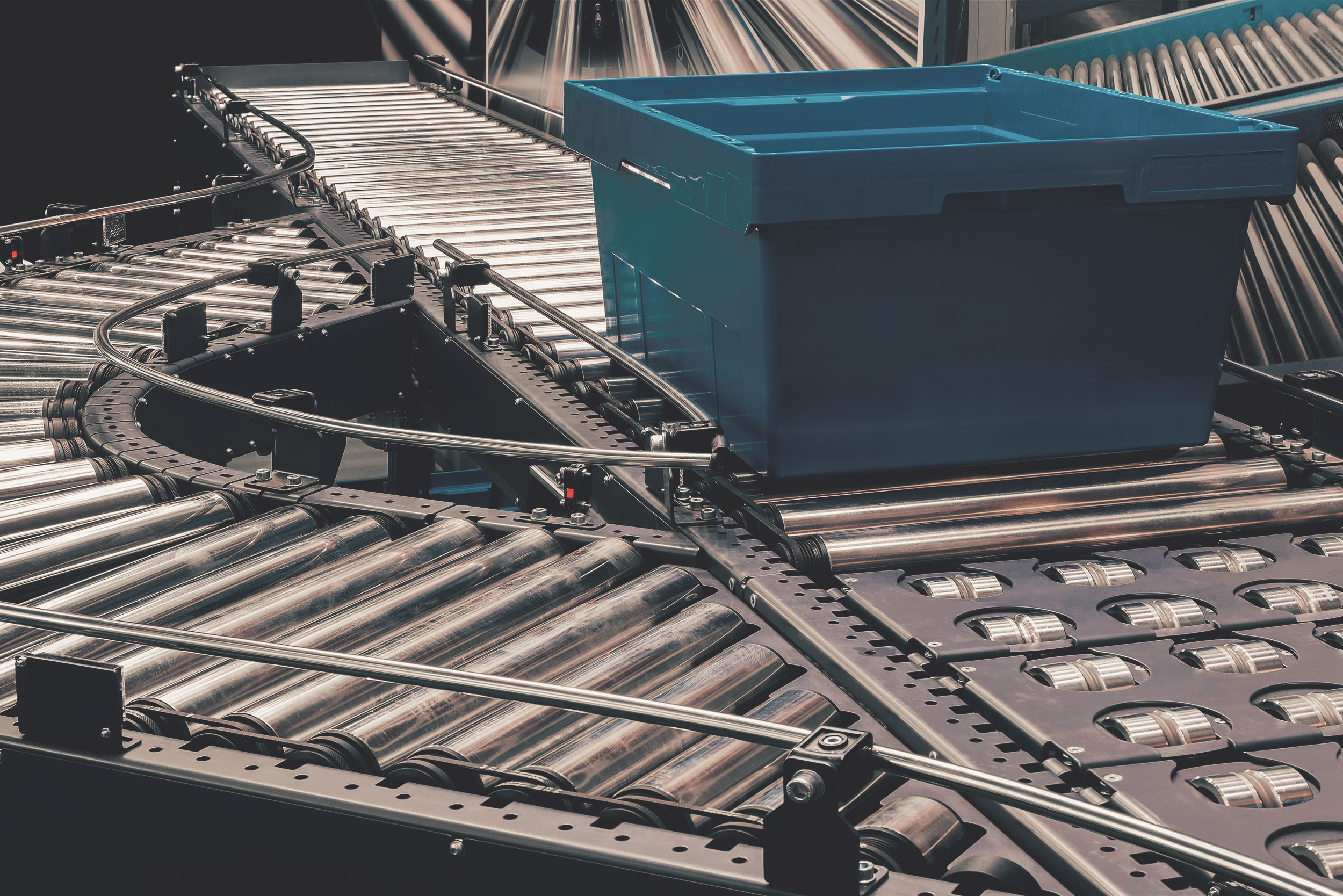 Blauer Kunststoffbehälter auf einem Förderband mit Rollen und Kettenantrieb in einer Logistikanlage